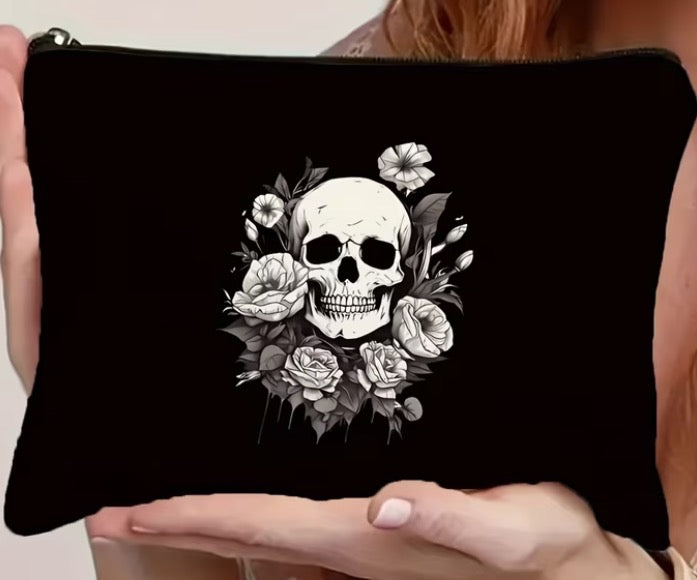 Black pouch with a skull and floral design held by a person.